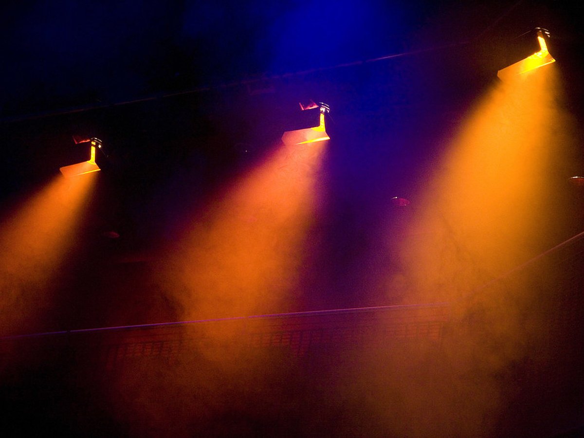 Iluminação cênica com feixes de luz e fumaça em palco de evento